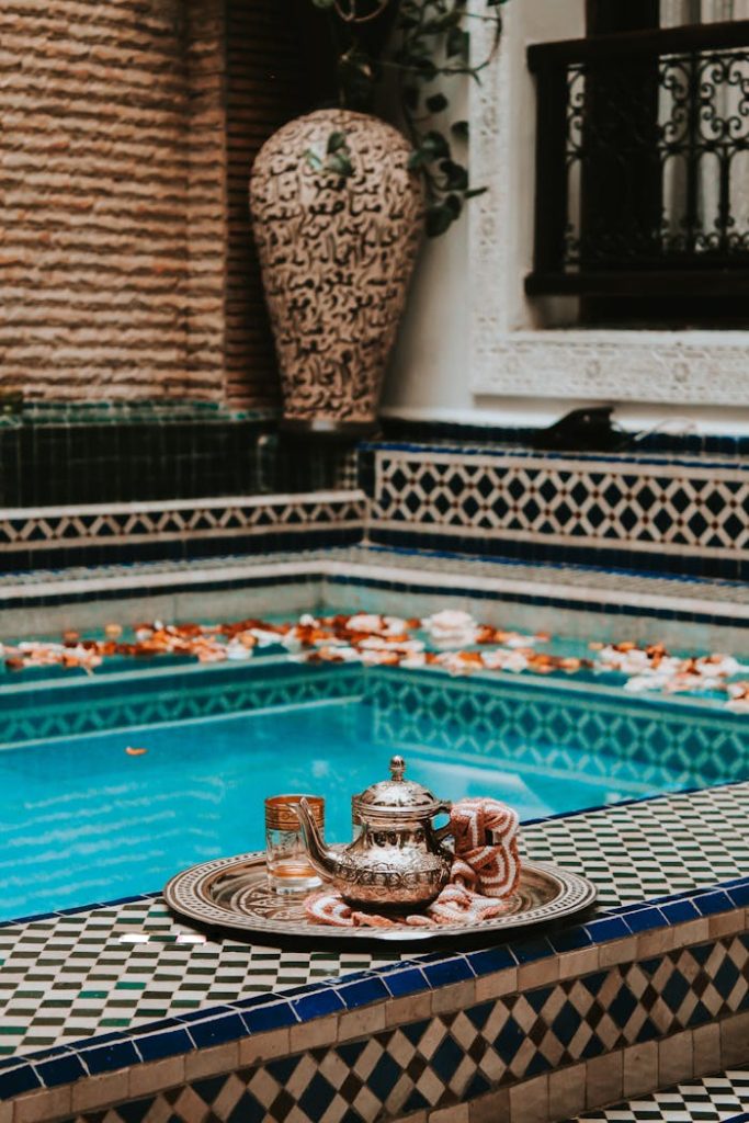 Home Elegant Moroccan tea setting by a vibrant pool with intricate tile designs in Marrakesh.
